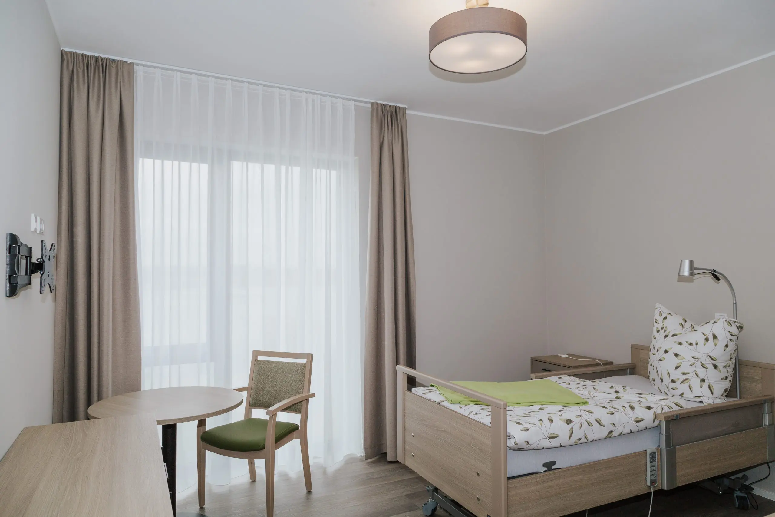 Stationäres Wohnen: Heller Wohnraum mit Pflegebett und Sitzbereich